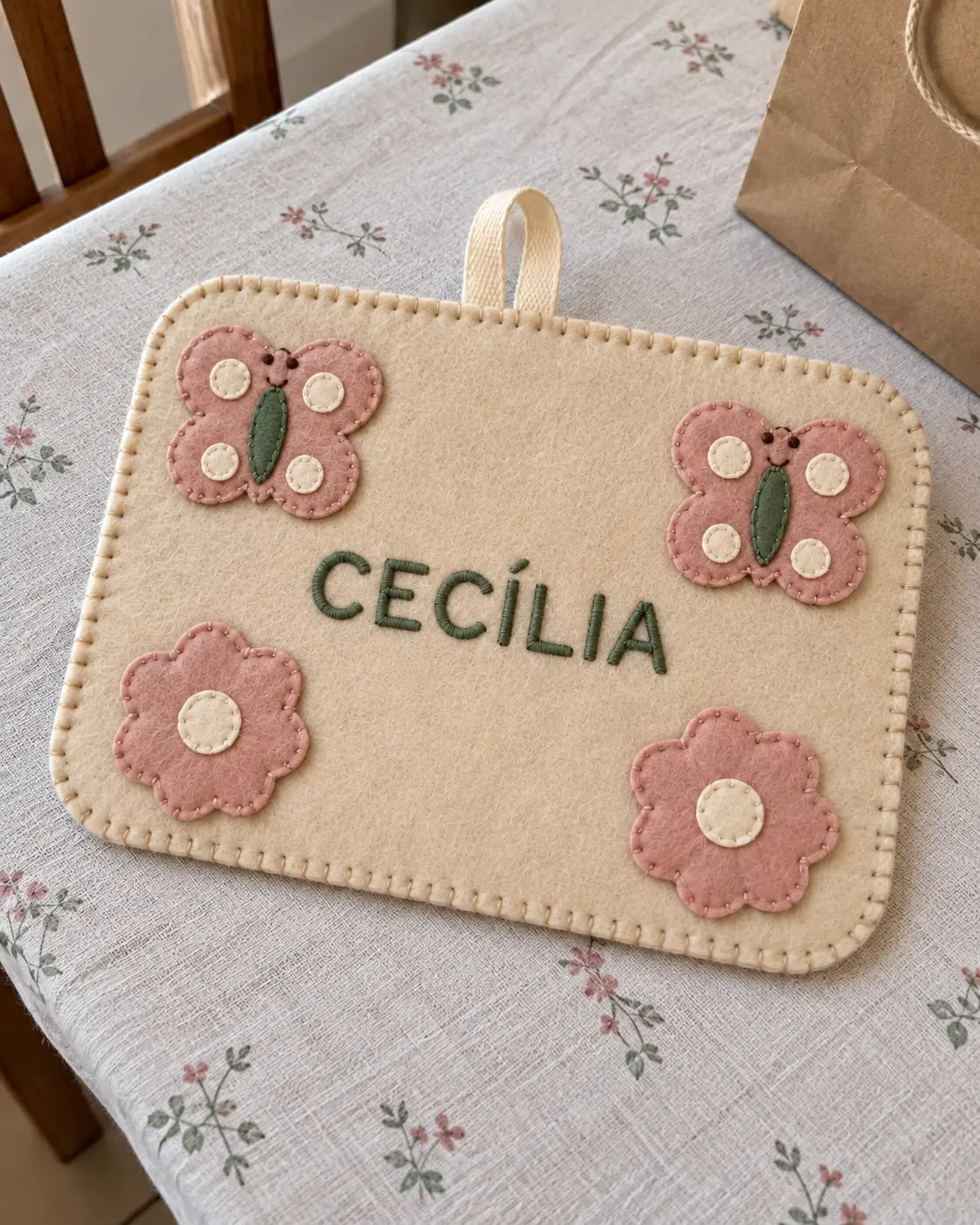 Placa de feltro com borboletas, flores e o nome CECÍLIA sobre a mesa